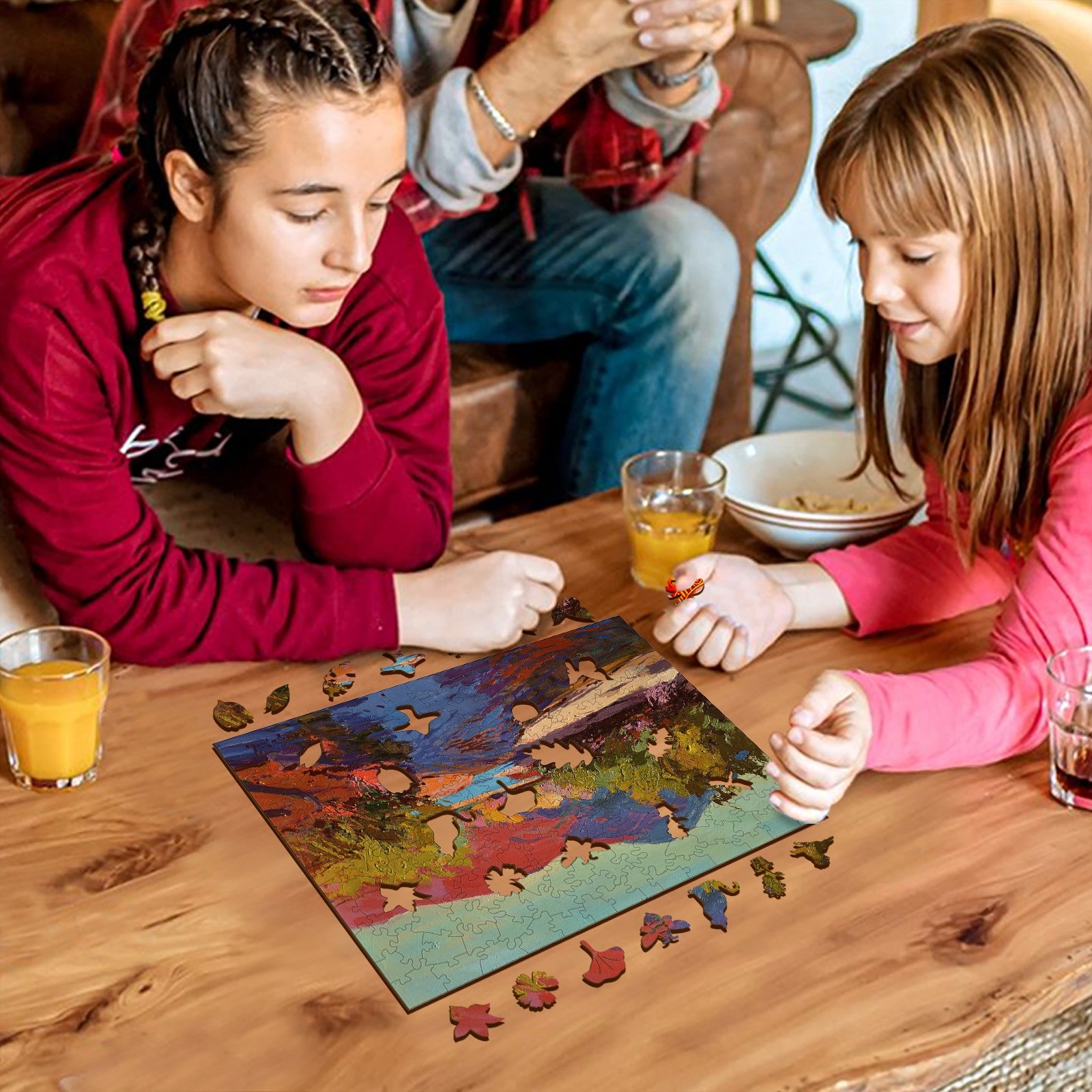 Two girls enjoying a puzzle inspired by artist Alexander Shandor, surrounded by drinks and a cozy setting.