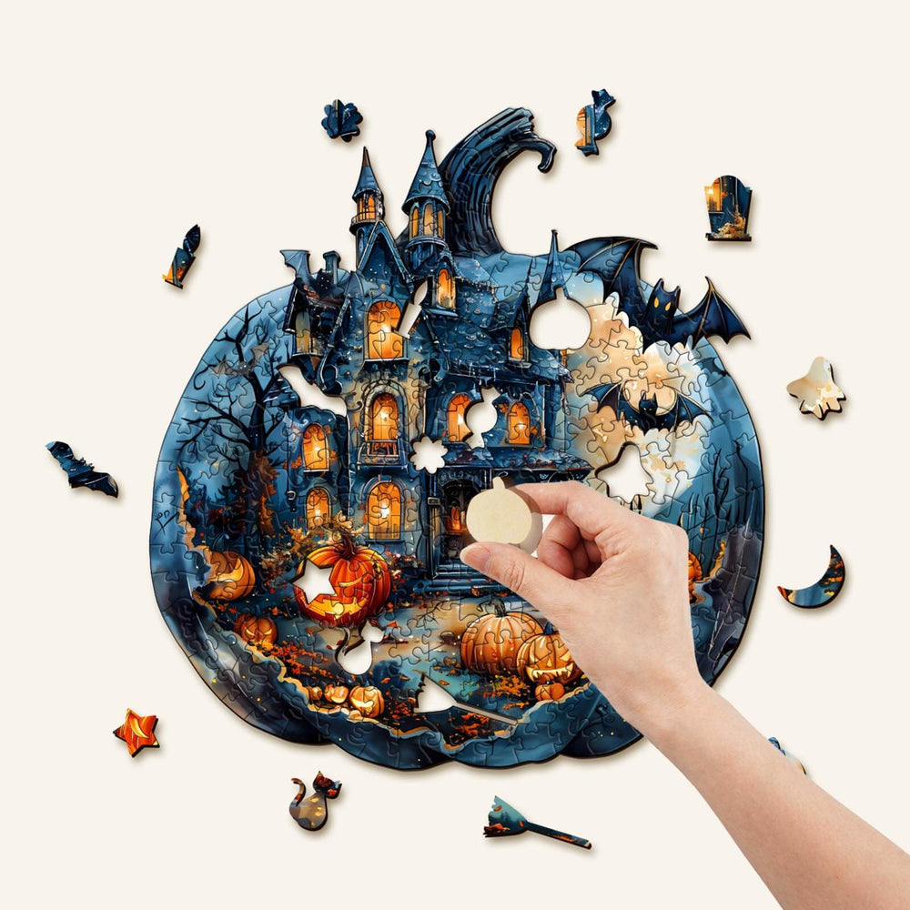 Hand placing a piece into a Halloween Pumpkin wooden jigsaw puzzle featuring a spooky castle and bats.