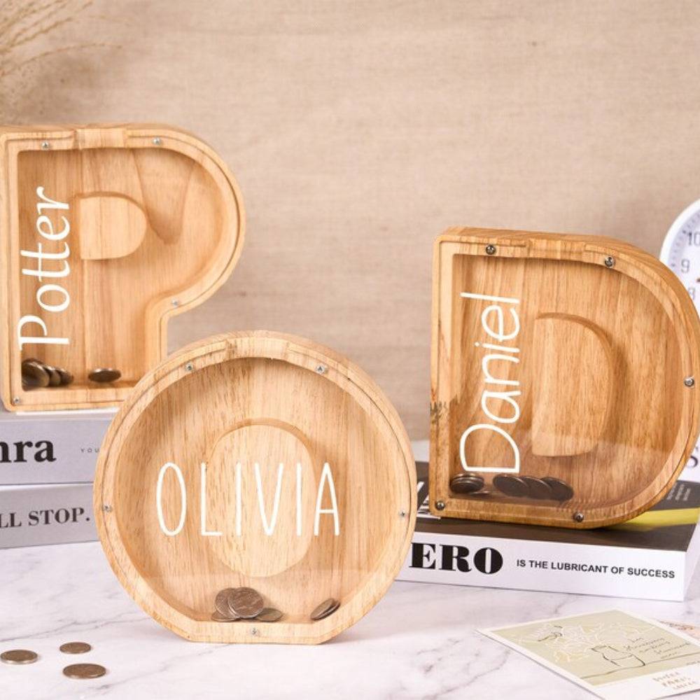 Personalized wooden letter piggy banks with names Potter, Olivia, and Daniel, promoting savings for kids.